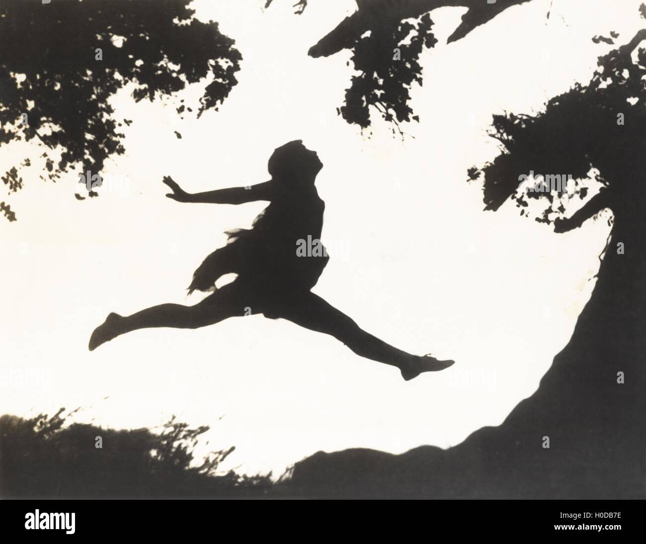 Silhouette of a woman in mid-air jumping between two trees Stock Photo