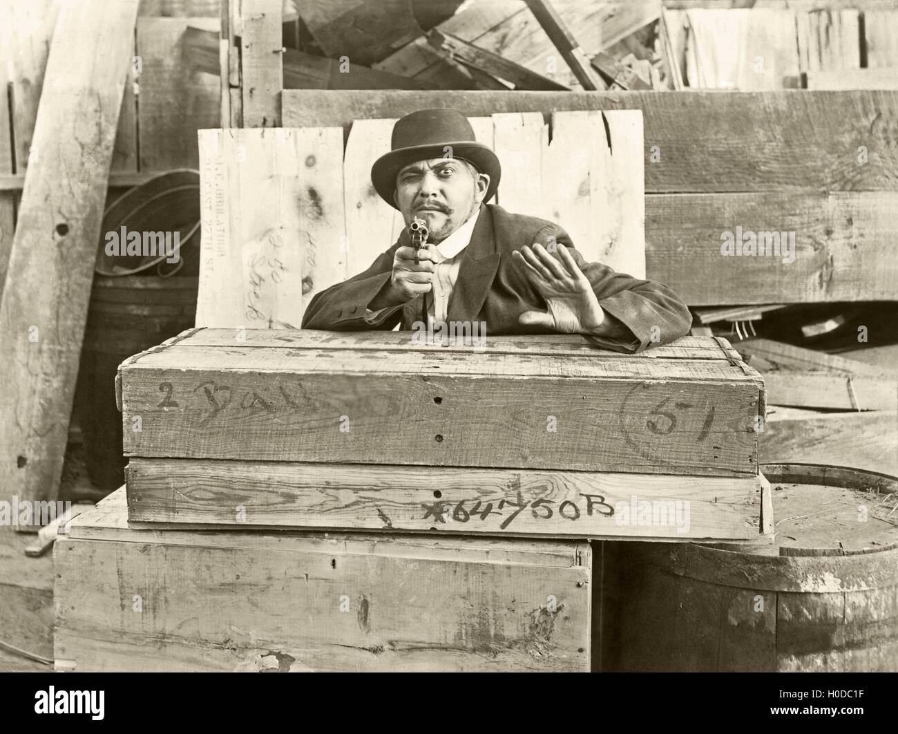 Cornered man behind wooden crates pointing gun Stock Photo