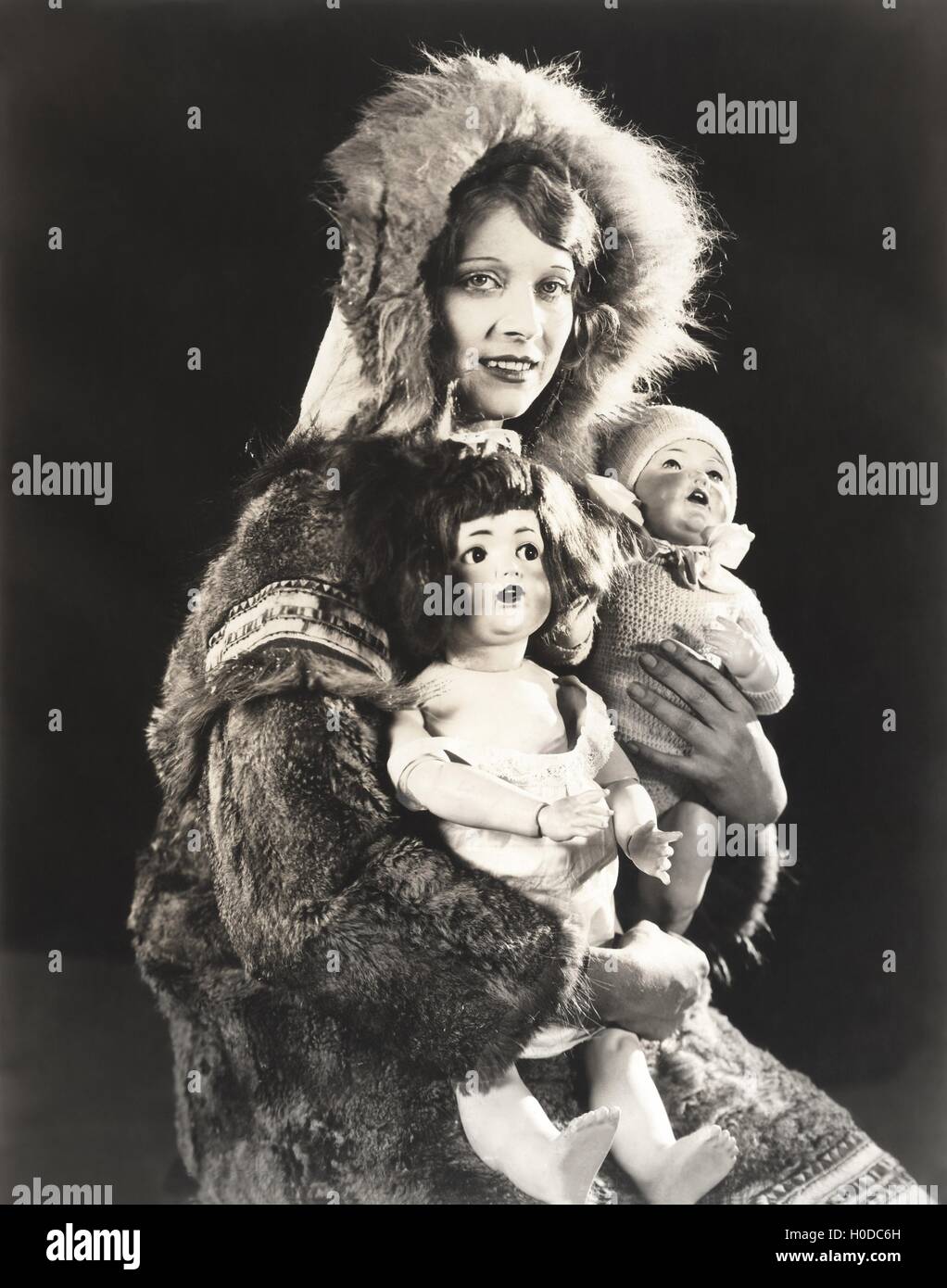 Women wearing Eskimo fur coat holding dolls Stock Photo