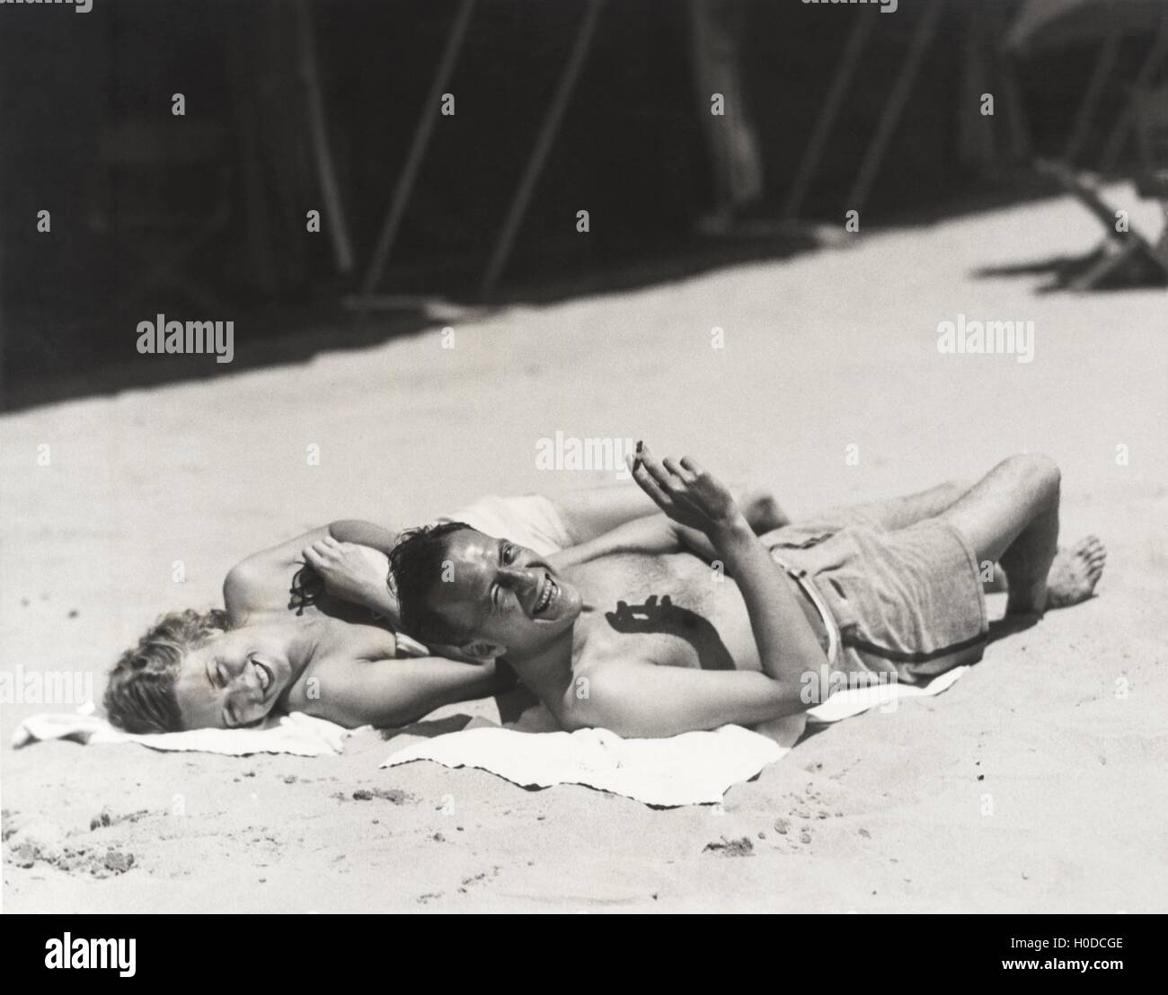 Happy couple sunbathing on beach Stock Photo