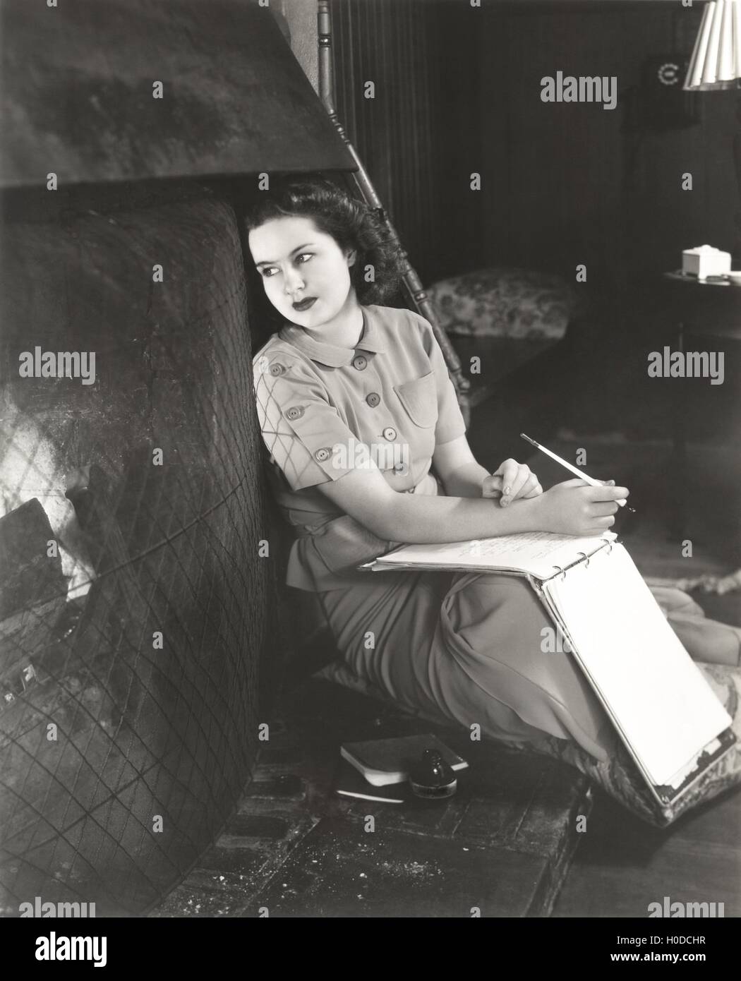 Woman with notebook daydreaming by fireplace Stock Photo