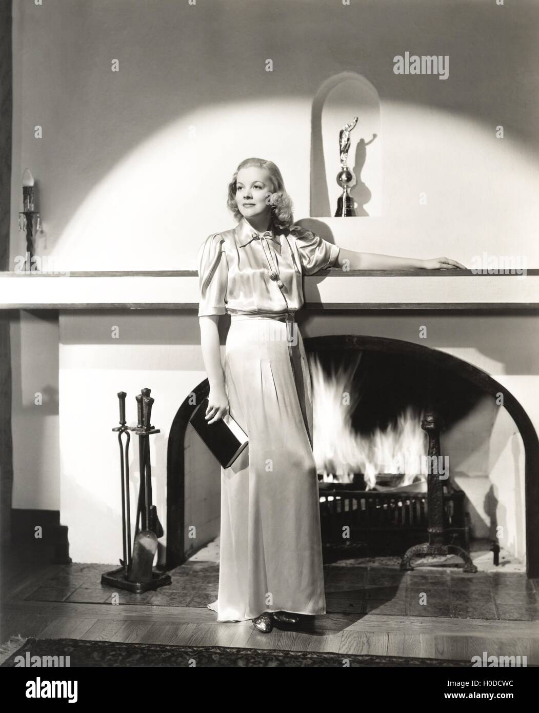 Woman in silk gown standing in front of fireplace Stock Photo