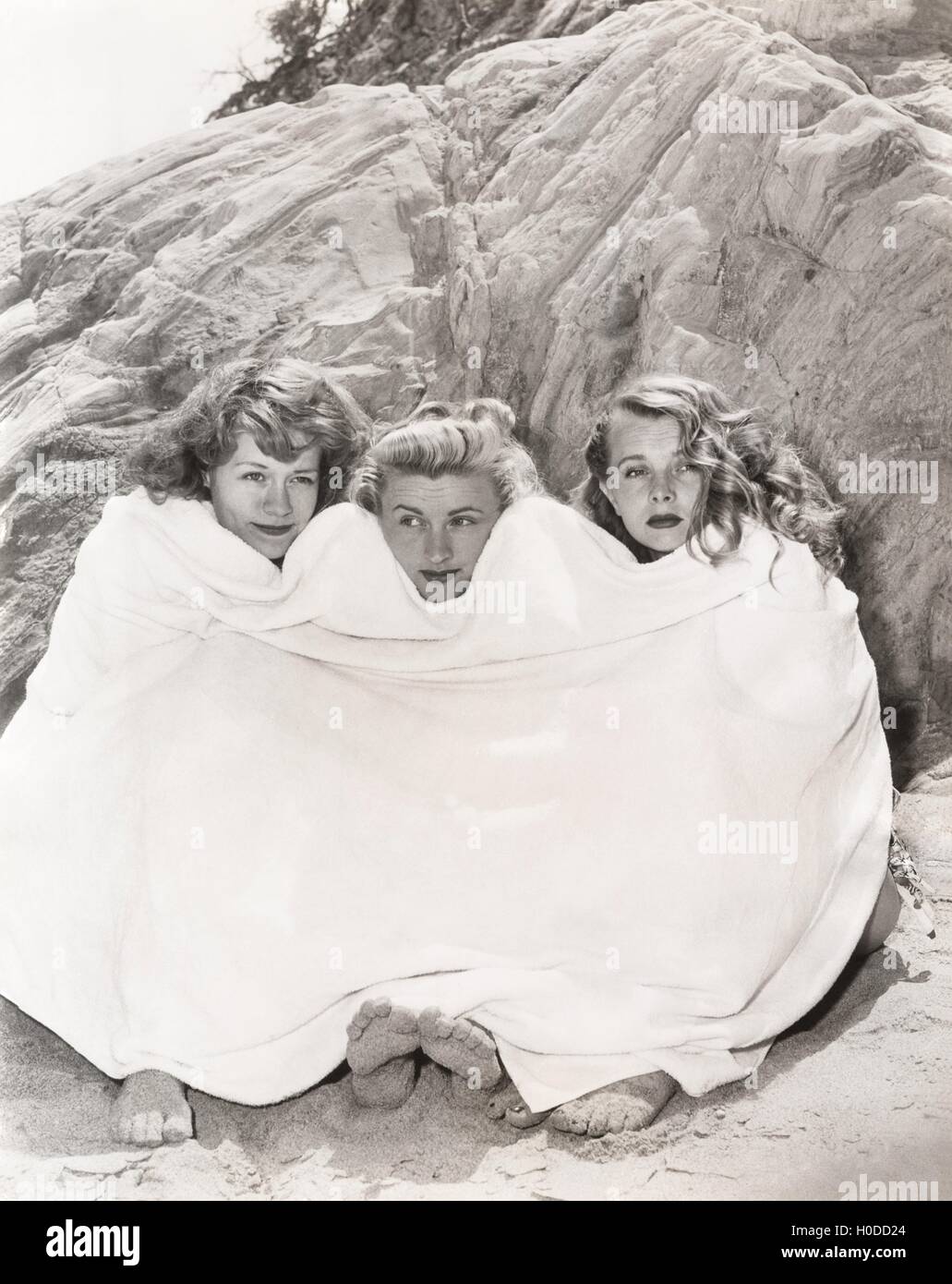 Three women huddled under a towel on beach Stock Photo