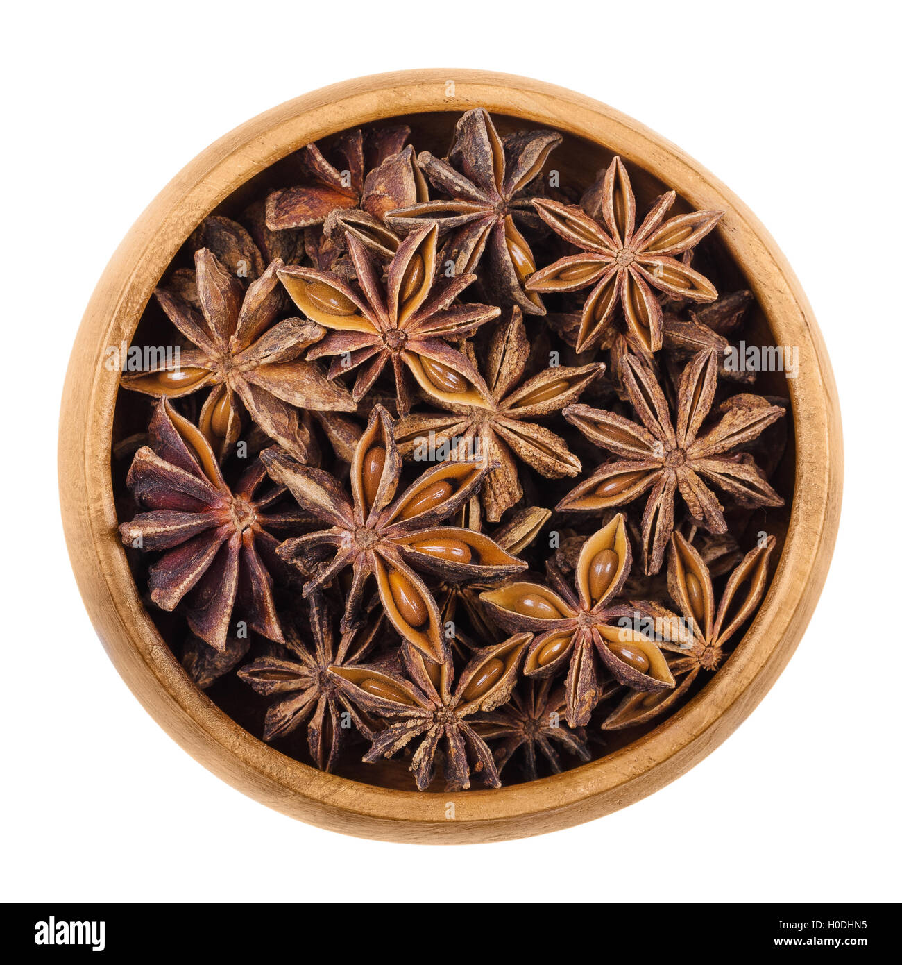 Star anise seeds in a wooden bowl over white. Dried fruits of Illicium verum, also Chinese star anise or badiam. Stock Photo