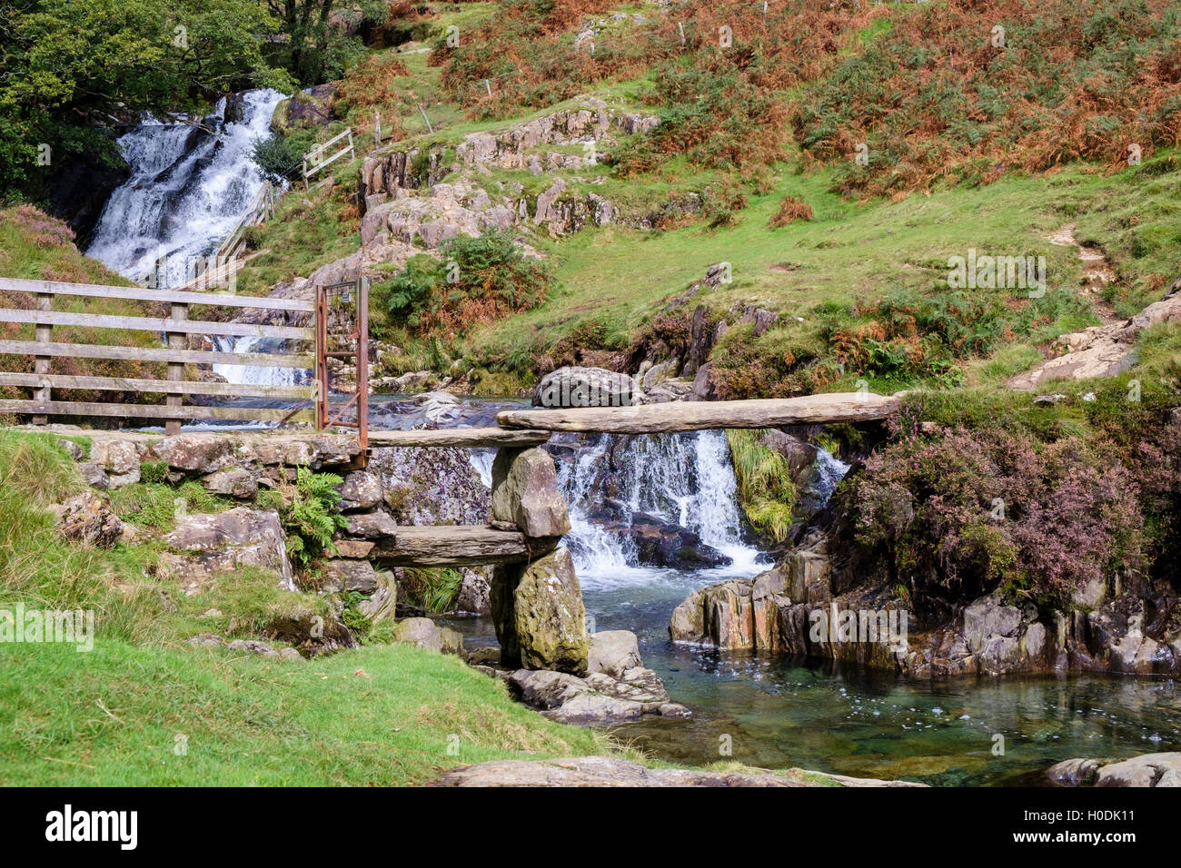 Old stone clapper footbridge on path crossing Afon Cwm Llan river below waterfall in Snowdonia National Park. Wales, UK Stock Photo