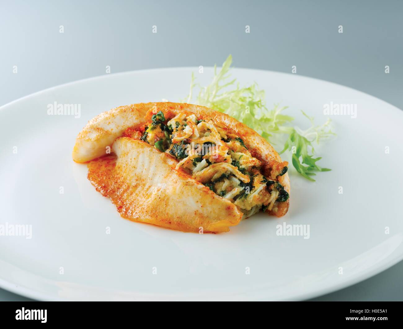 Fried stuffed tilapia with lettuce on white plate in restaurant Stock