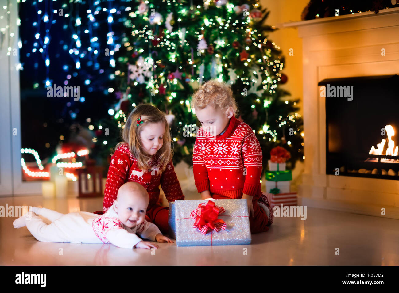Family on Christmas eve at fireplace. Kids opening Xmas presents