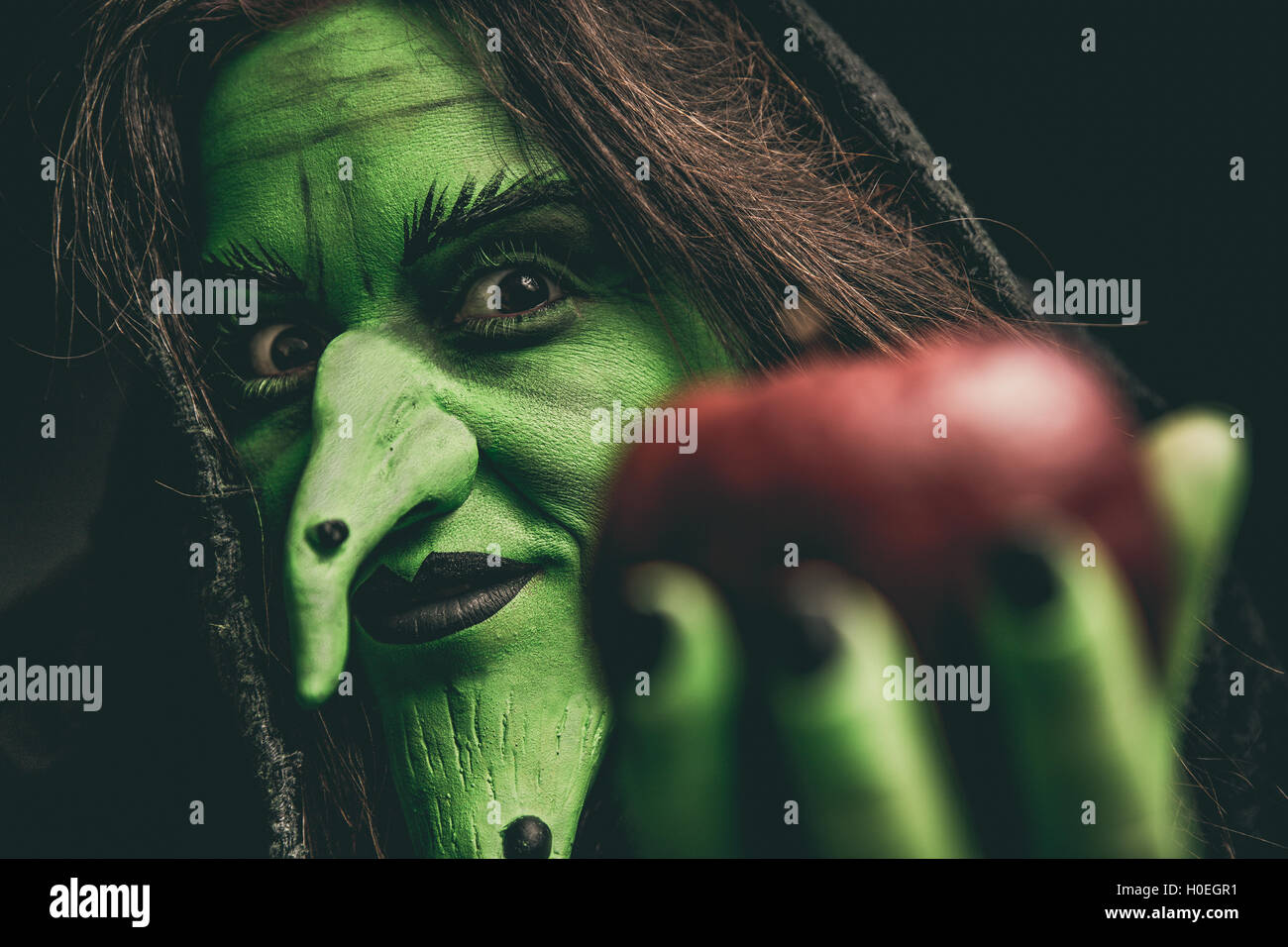 Green witch holding an apple in her hand. Shallow depth of field. Stock Photo