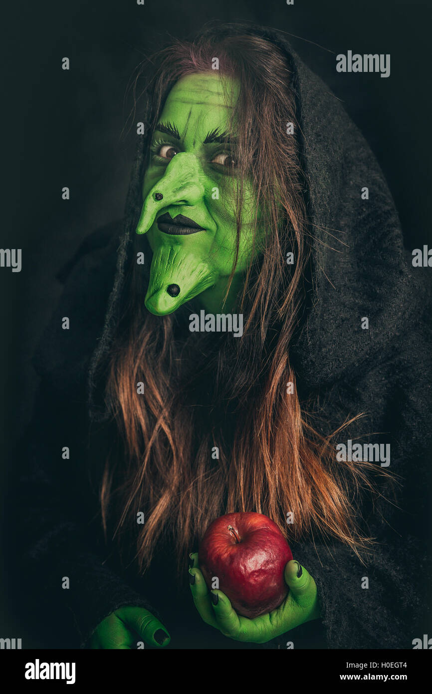 Green witch with long hair holding a rotten apple in her hand Stock Photo