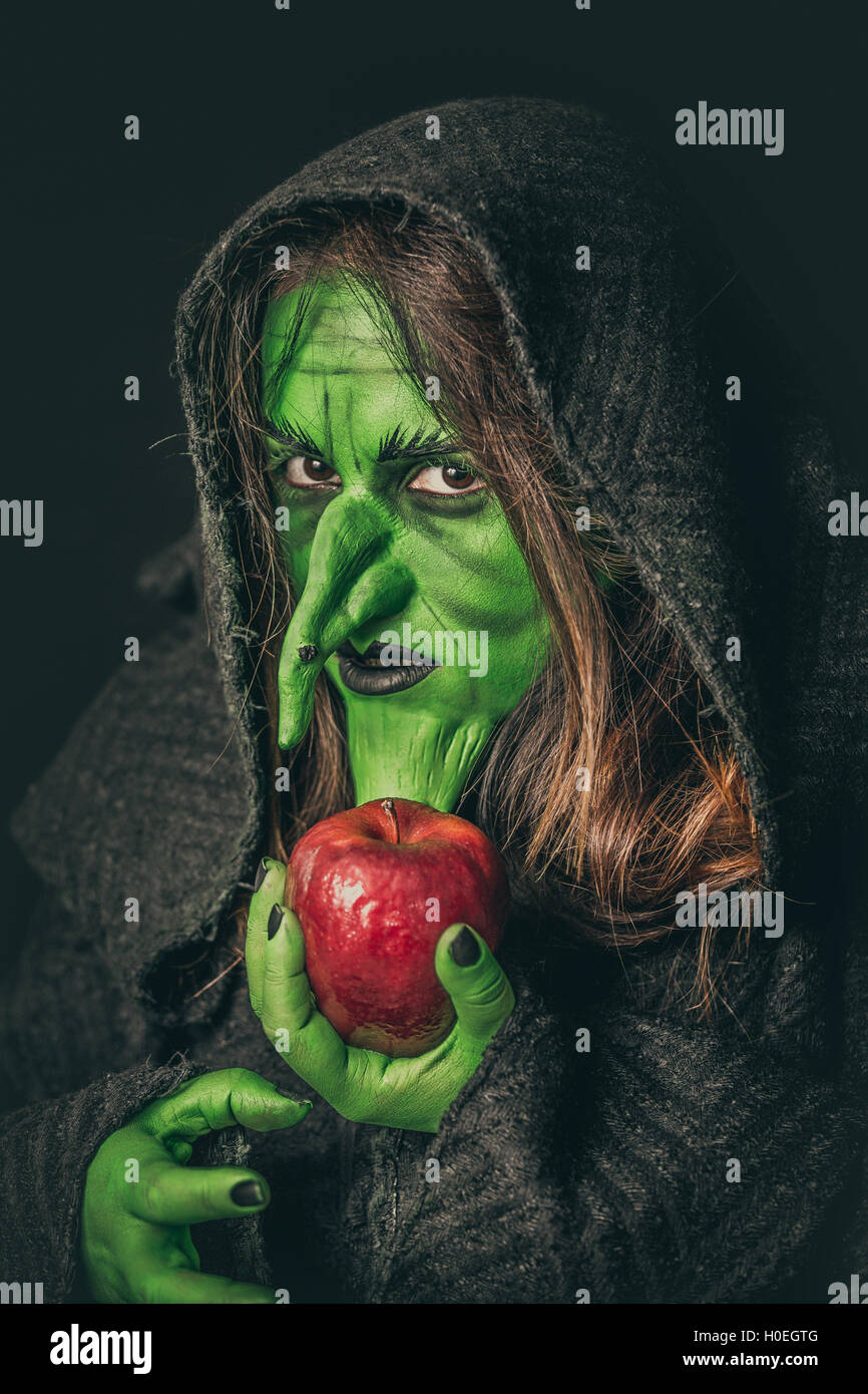 Angry witch with long hair holding a rotten apple in her hand Stock Photo