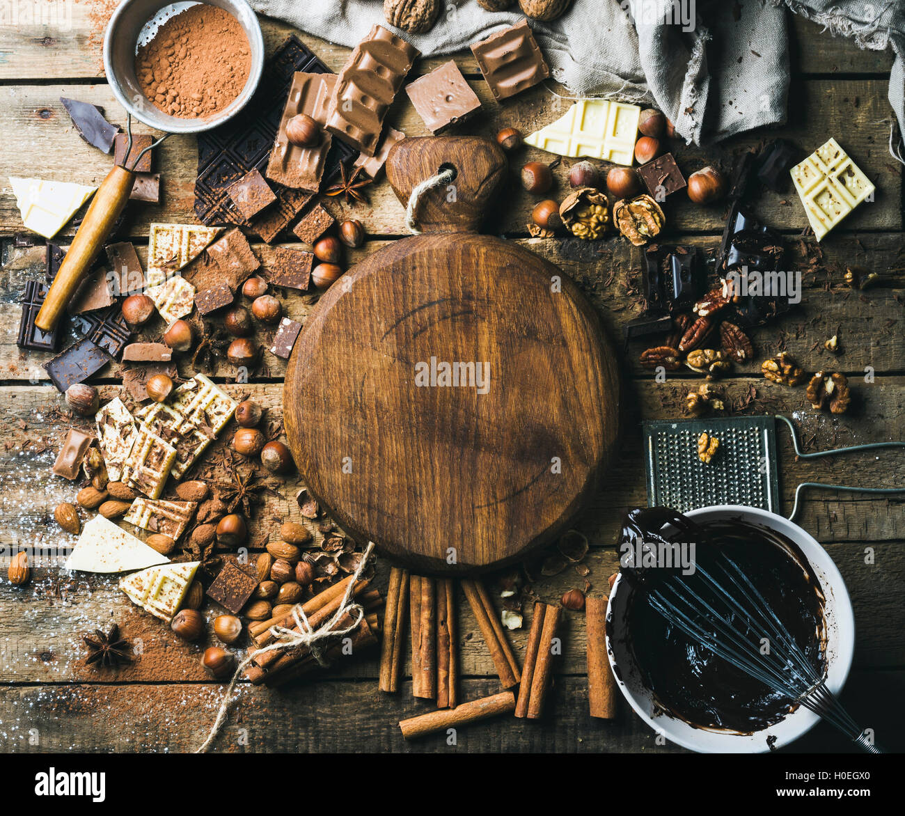 Pieces of white, dark and milk chocolate, nuts, cocoa powder, melted chocolate and spices with wooden board in center. Hot choco Stock Photo