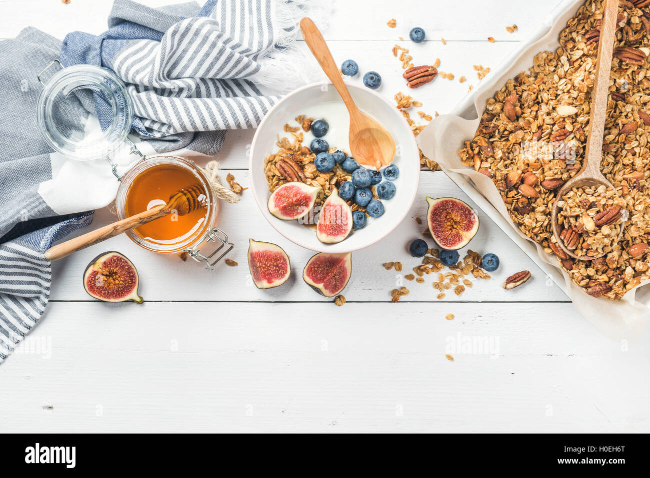 Healthy breakfast set. Oat granola with nuts, yogurt, honey, fresh figs and blueberries in bowl on white wooden background, top Stock Photo