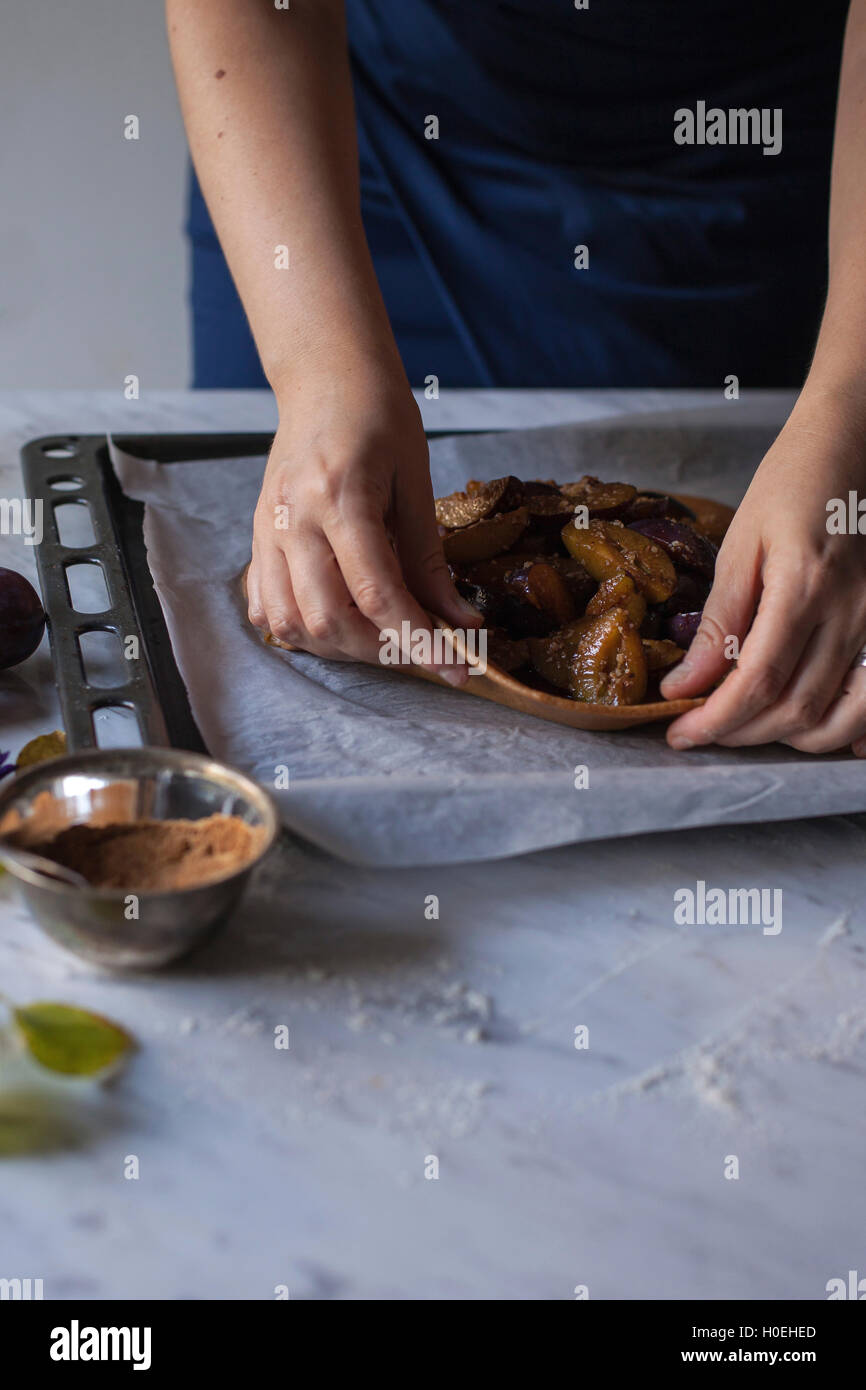 Woman folding dough over sliced plums, ingredients for baking plum