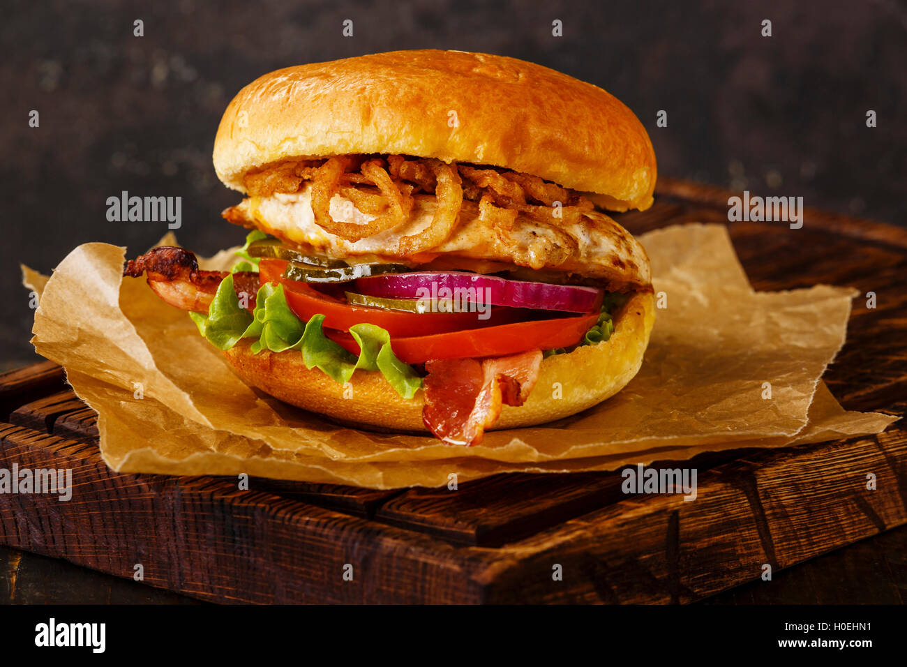 Burger with chicken breast and fried onions on dark background Stock Photo