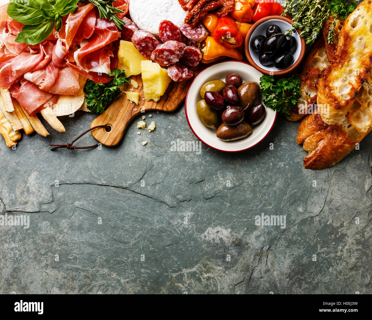 Italian food ingredients background with ham, salami, parmesan, olives, bread sticks on stone slate Stock Photo