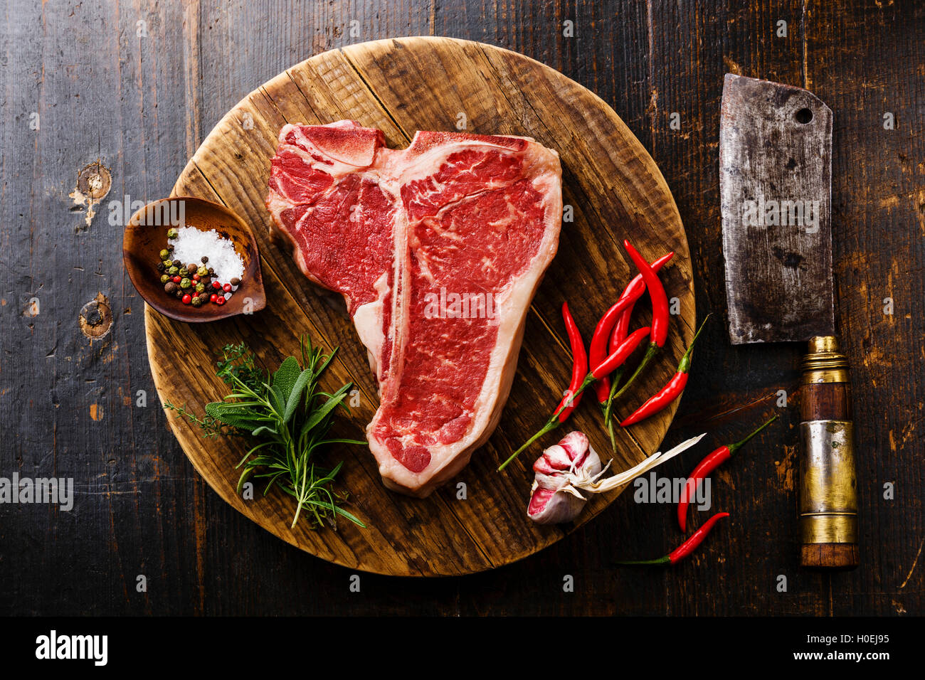 Raw fresh meat T-bone steak, seasoning and Butcher cleaver on chopping cutting board on wooden background Stock Photo