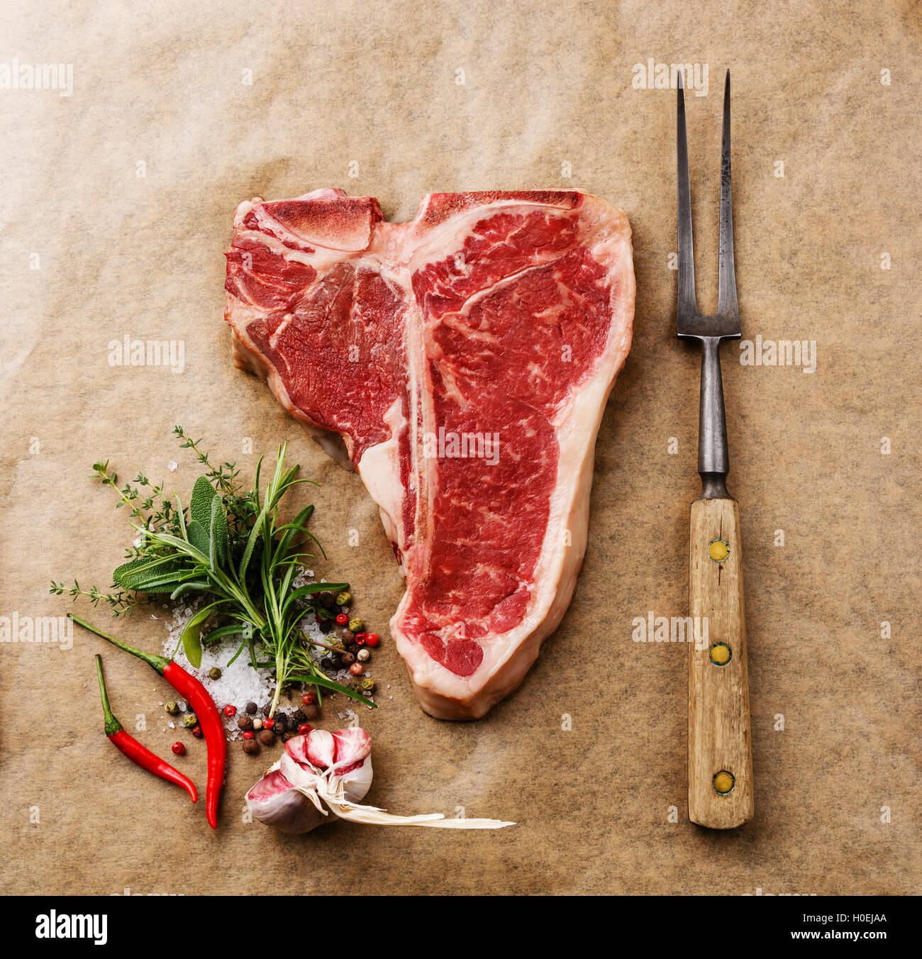 Raw fresh meat T-bone steak, seasoning and meat fork on cooking paper background Stock Photo