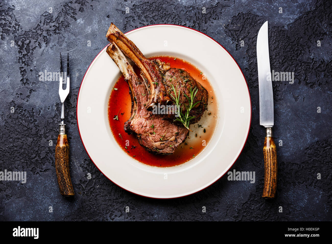 Roasted beef ribs on bone on plate with knife and fork carving set on dark background Stock Photo