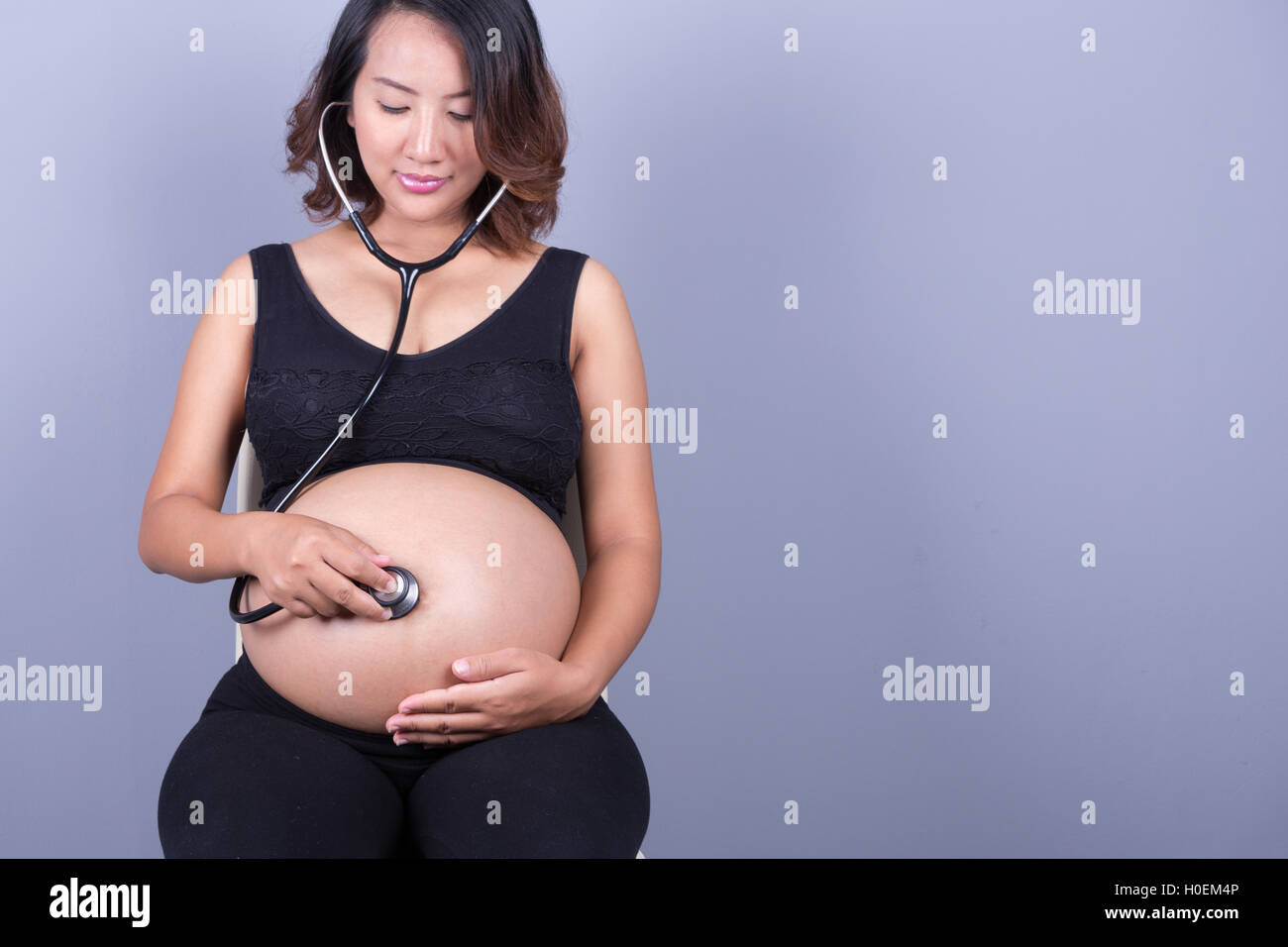 pretty young pregnant asian woman with stethoscope listening belly to baby Stock Photo