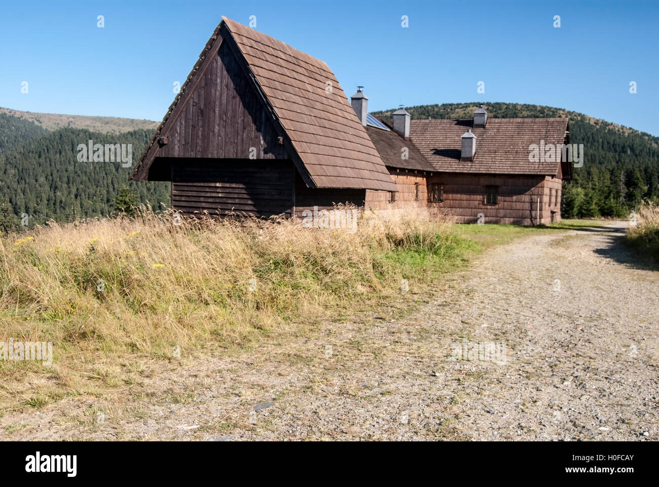 Frantiskova myslivna wooden hut in summer Jeseniky mountains with dirty road, hill on the background and clear sky Stock Photo
