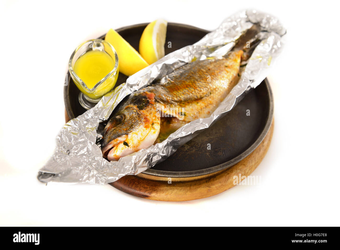 Grilled fish in foil uith lemon juice sauce in black pan on wooden cutting board Stock Photo
