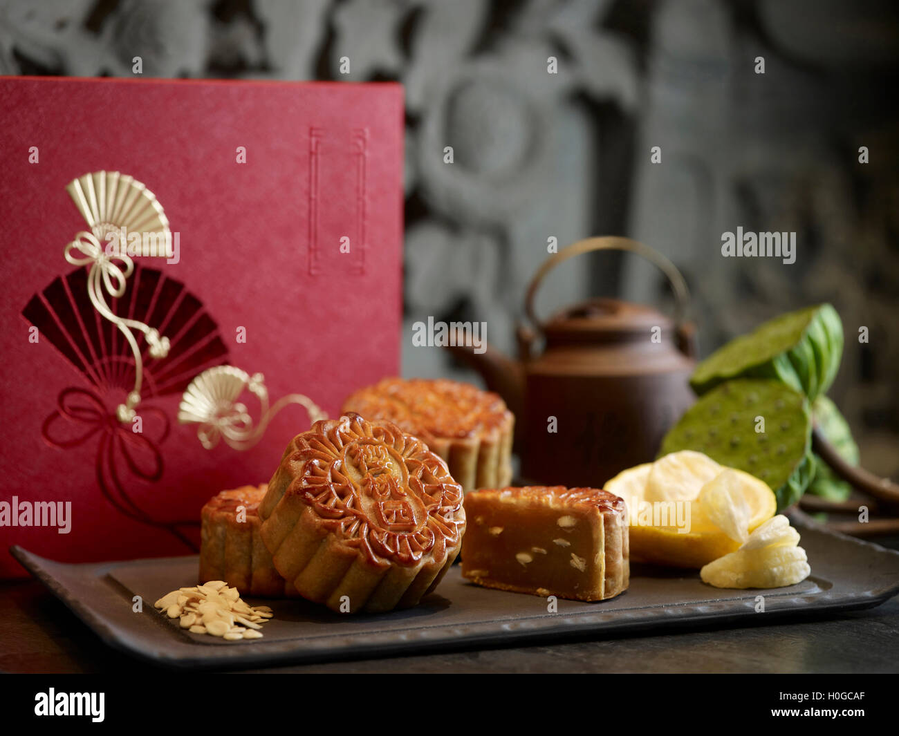 Oriental mooncake with silver lotus paste yuzu and melon seeds on black platter with tea pot