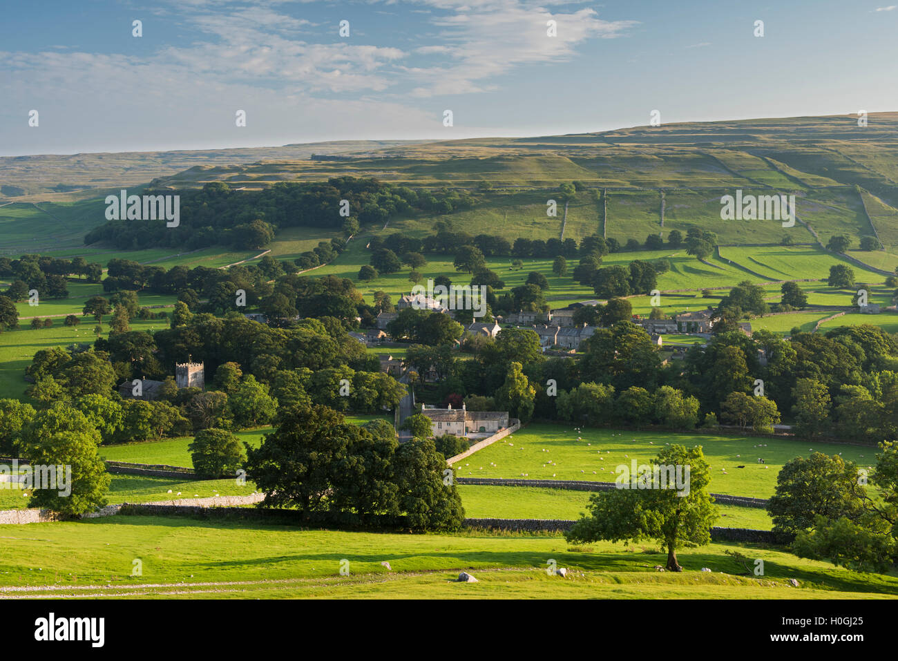 Summer evening view over picturesque Dales village of Arncliffe (church & houses) nestling in valley under sunlit hills - North Yorkshire, England, UK Stock Photo