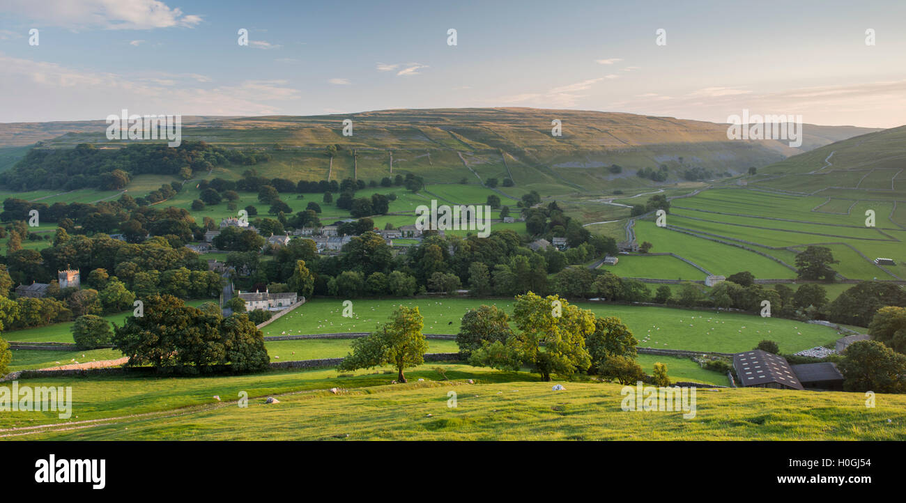 Summer evening view over picturesque Dales village of Arncliffe (church & houses) nestling in valley under sunlit hills - North Yorkshire, England, UK Stock Photo