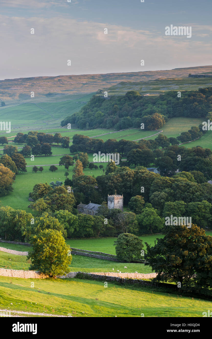 Summer evening view over church (& tower) in picturesque Dales village nestling in valley under sunlit hills - Arncliffe, North Yorkshire, England, UK Stock Photo