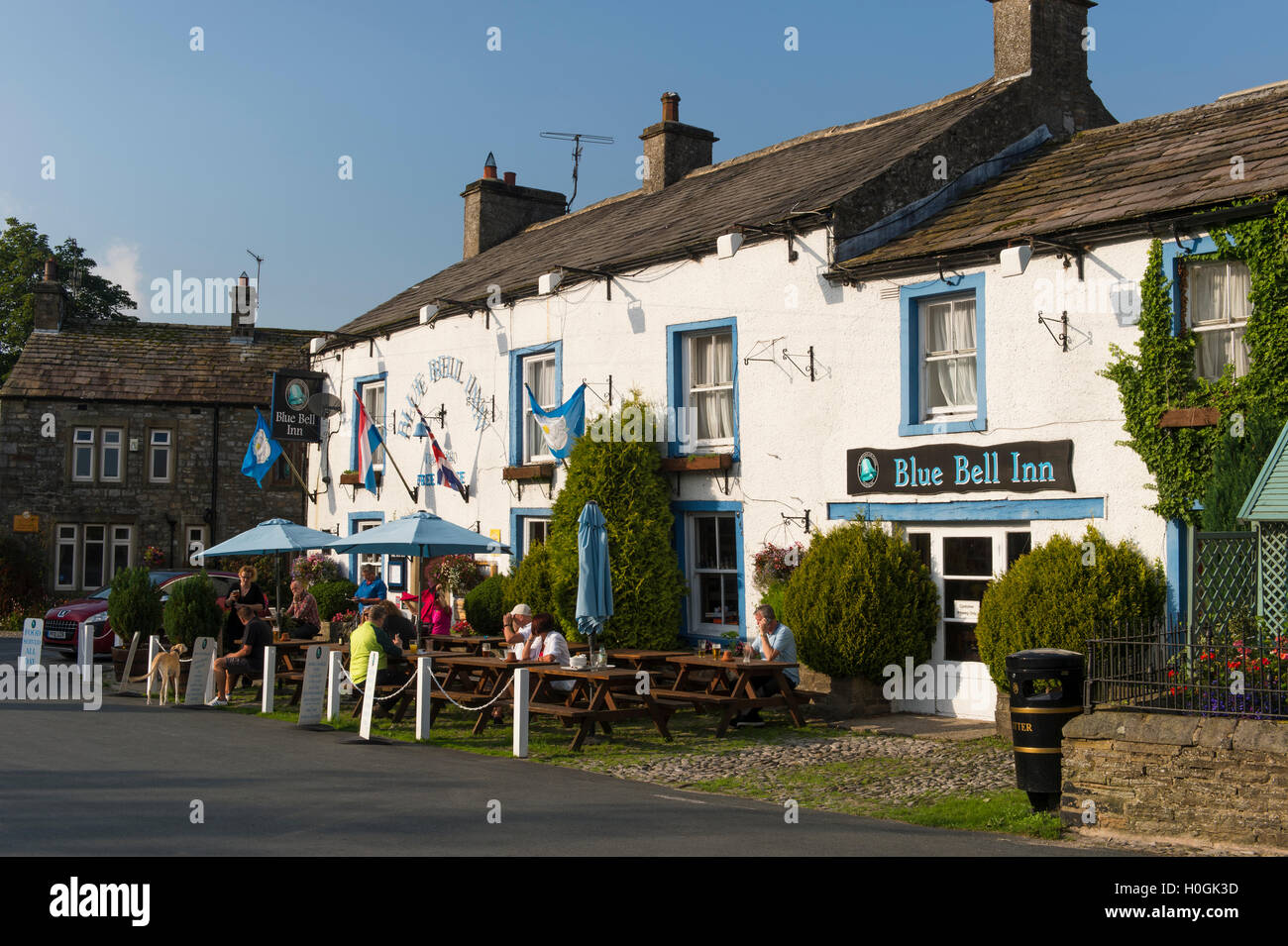 People eat & drink al fresco in the sun at attractive, traditional English pub - The Blue Bell Inn, Kettlewell village, Yorkshire Dales, England, UK. Stock Photo