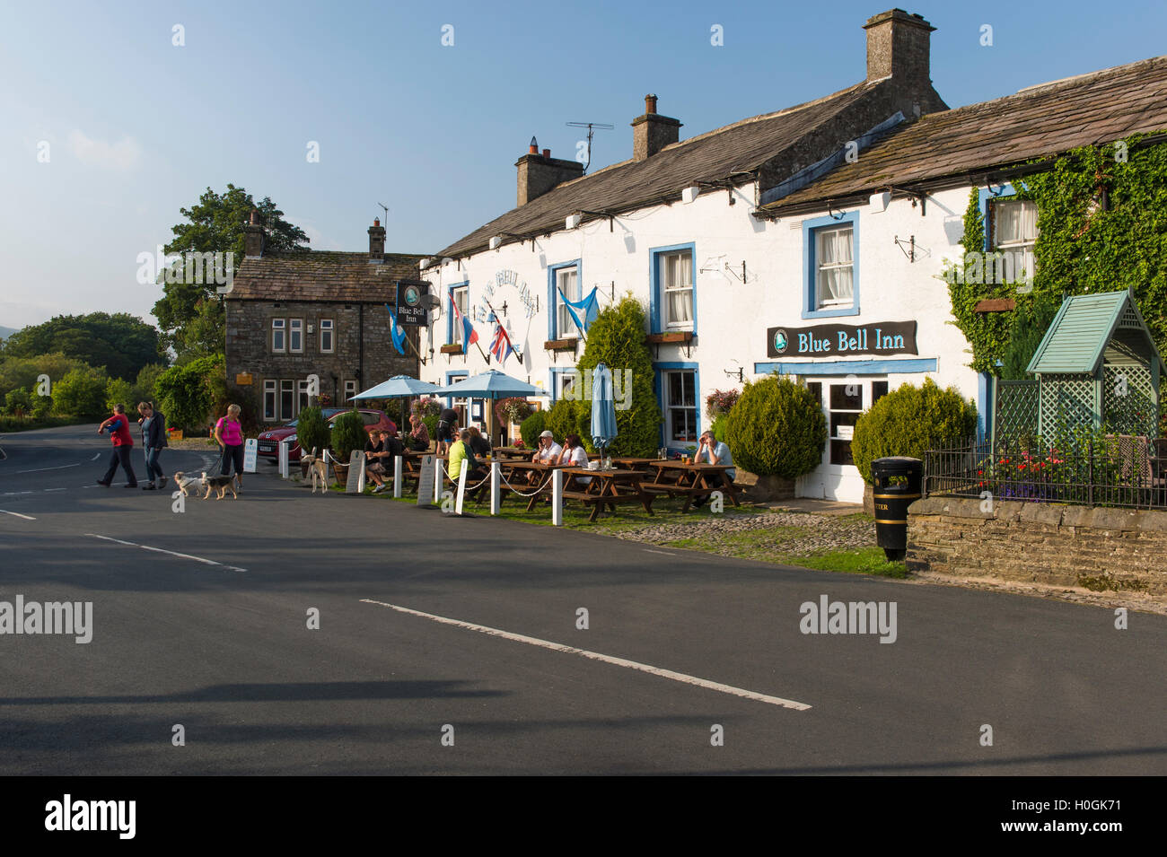 People eat & drink al fresco in the sun at attractive, traditional English pub - The Blue Bell Inn, Kettlewell village, Yorkshire Dales, England, UK. Stock Photo