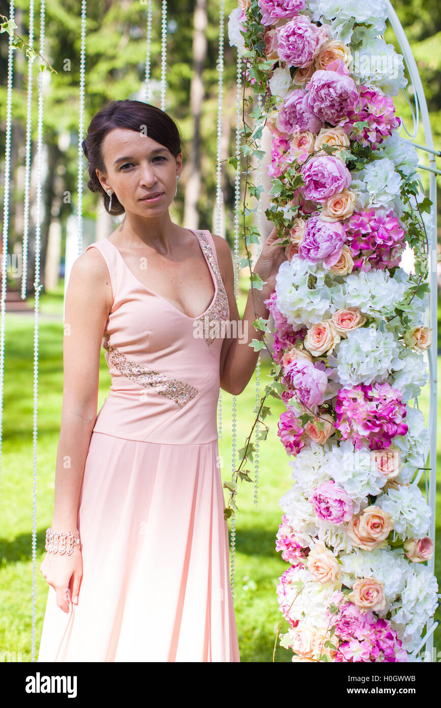 Beautiful young girl in long dress at the ceremony near flower arch Stock Photo