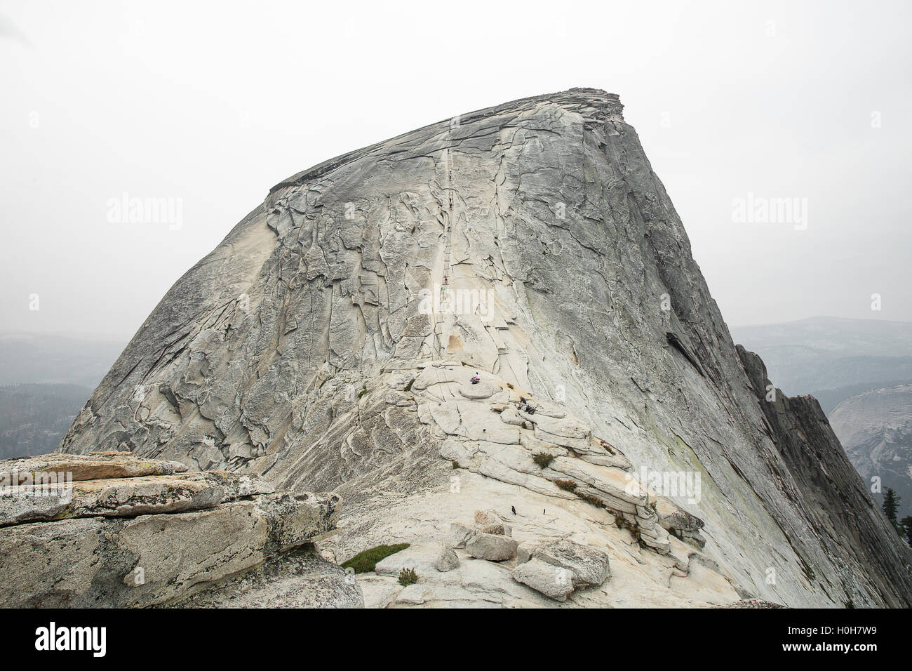 Hikers make their way up Yosemite's Half Dome, making sure to hold to the safety chain. Stock Photo