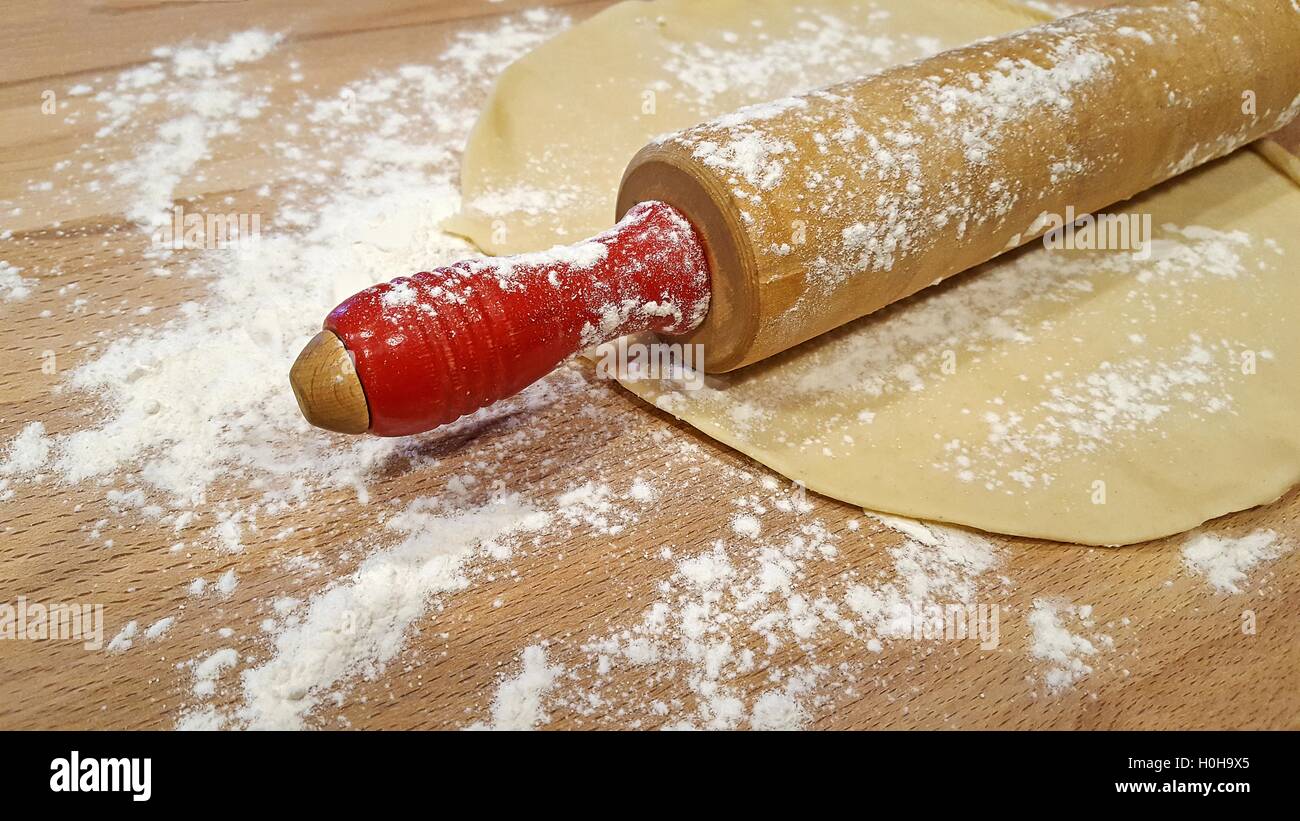 Retro wooden rolling pin with red handles on pie crust and flour Stock Photo