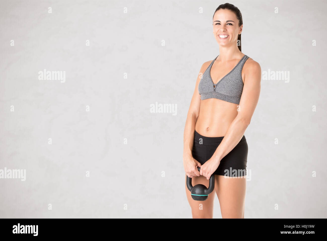 Fit woman working out with a kettlebel and similingl, isolated in grey Stock Photo