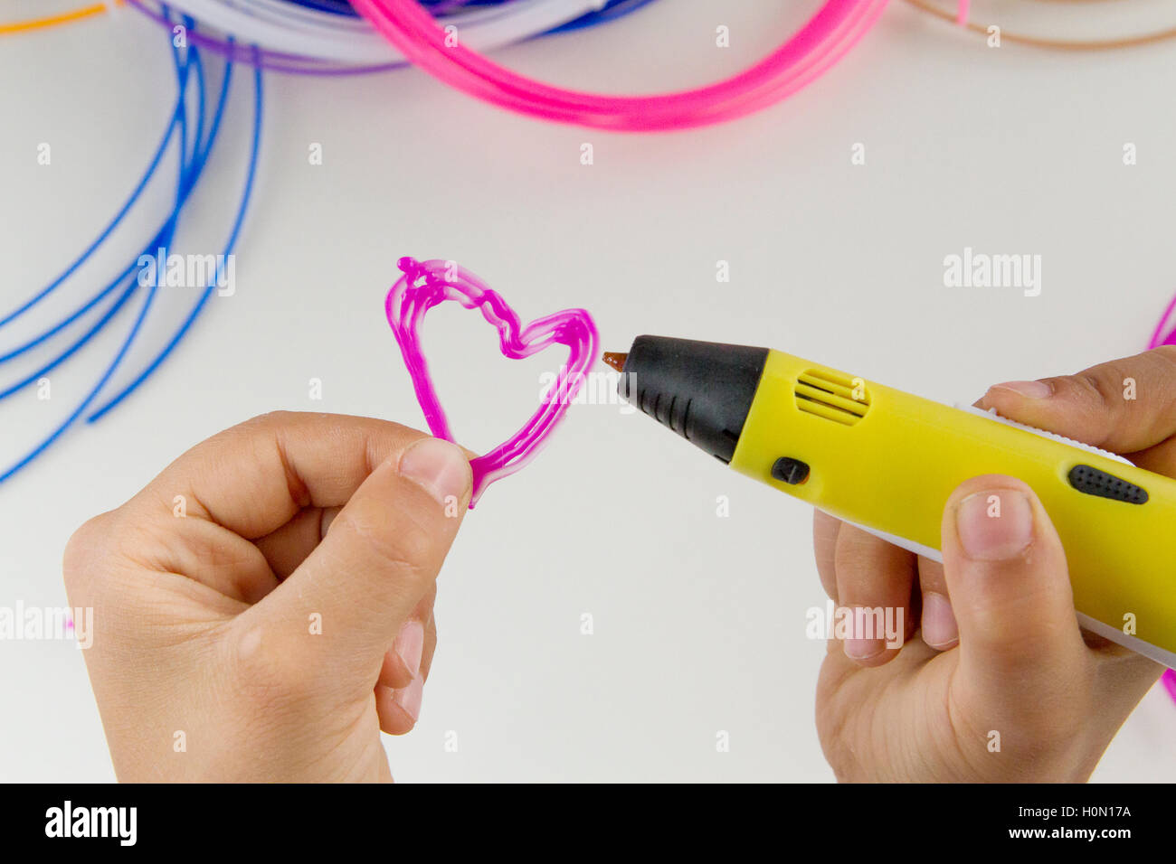 Child makes with 3d drawing pen a heart. Colourful filaments and white background. Top view. Close up Stock Photo