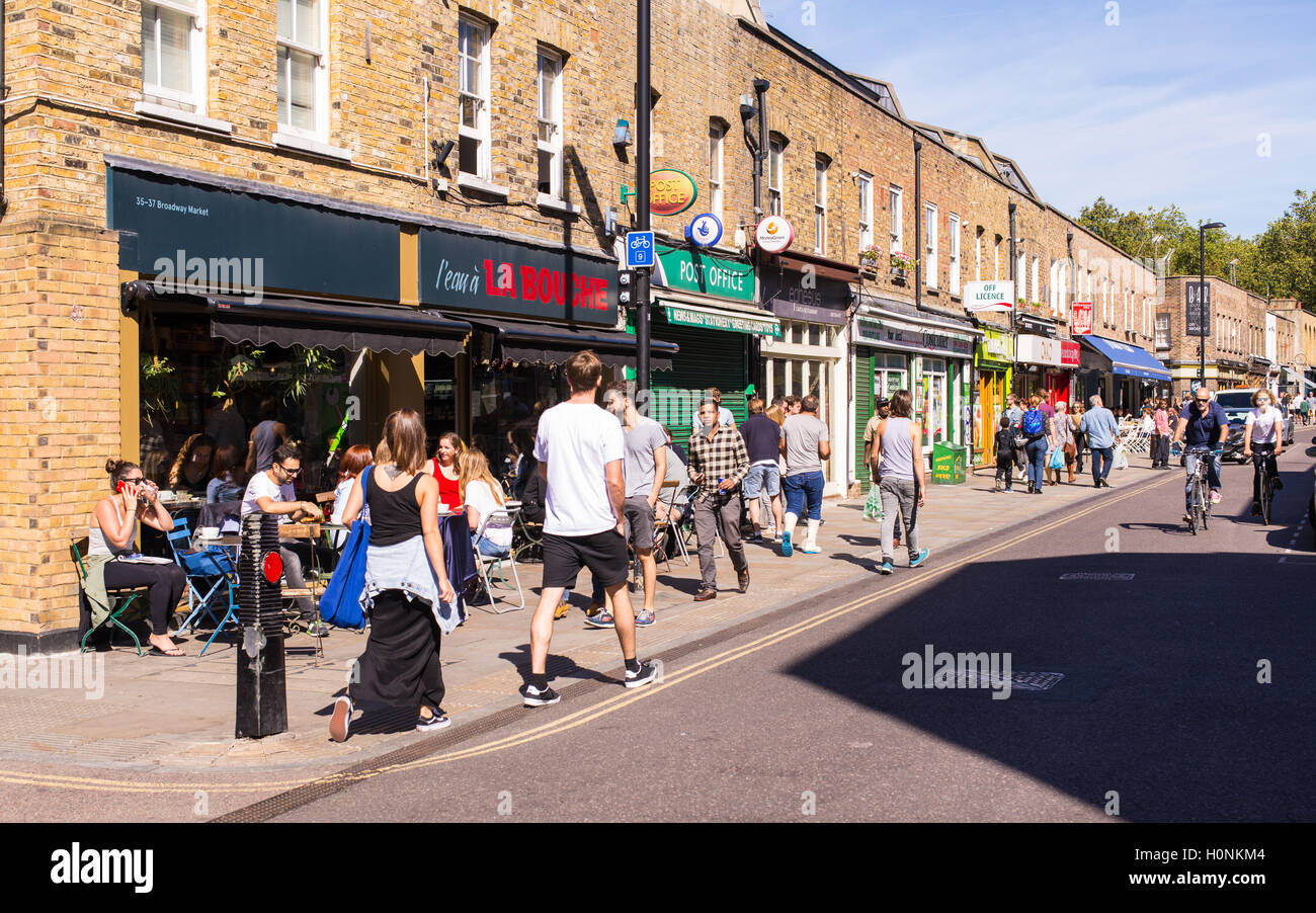 People walking in front of local shops and restaurants in Broadway Market, East London, on a sunny day. Stock Photo