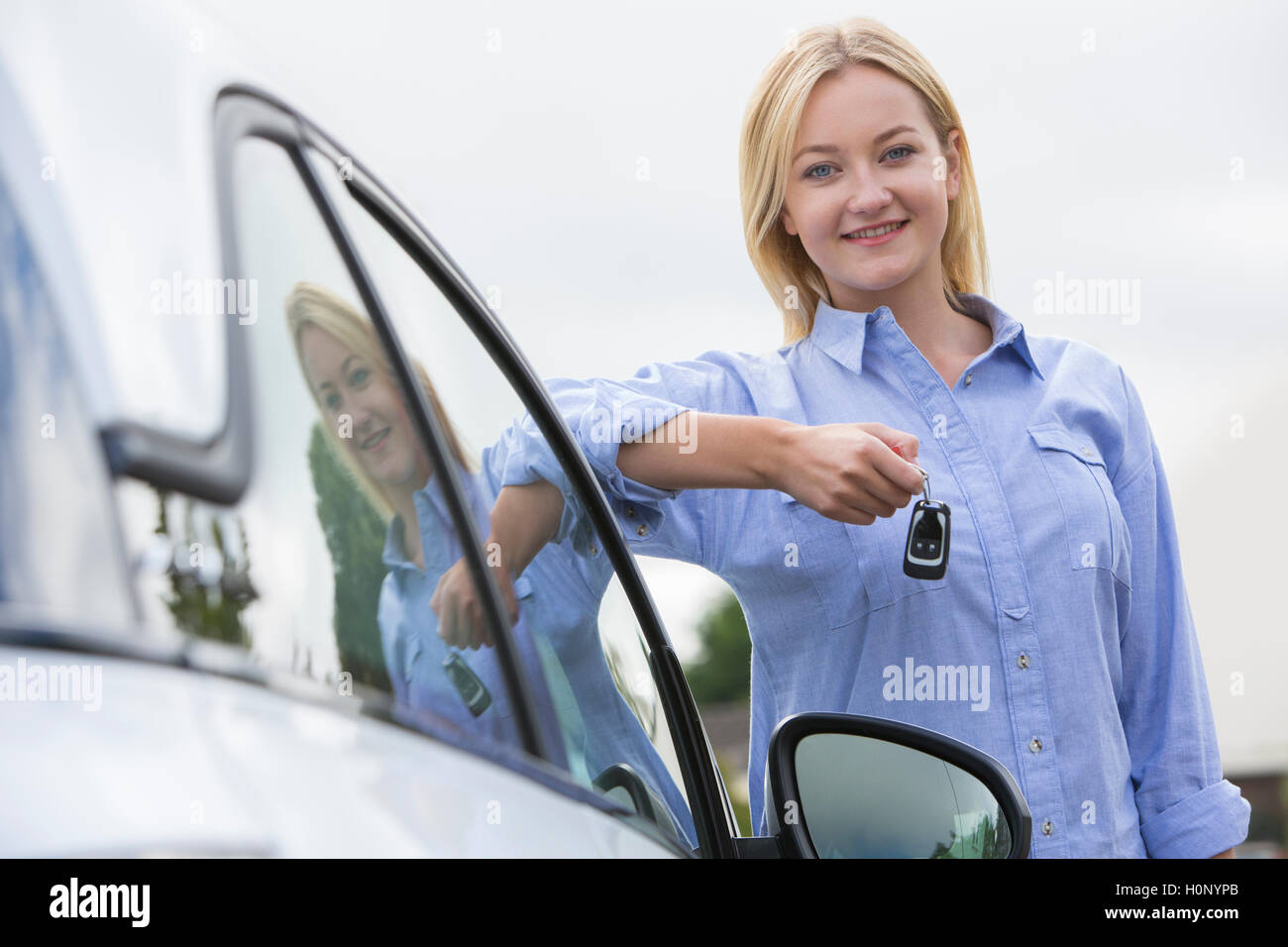 Young Female Driver Holding Car Keys Next To Vehicle Stock Photo