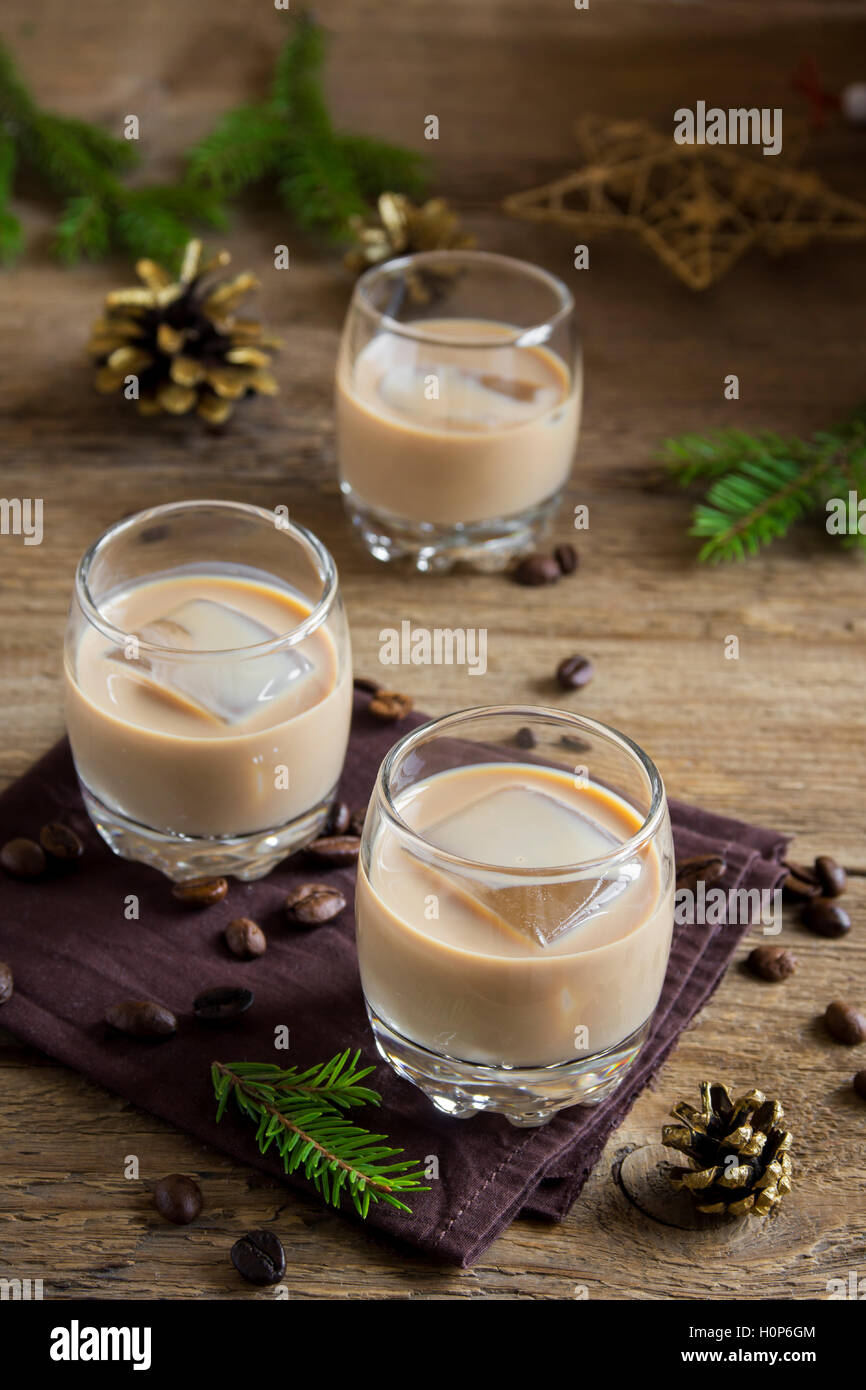 Irish cream coffee liqueur with ice, Christmas decoration and ornaments over rustic wooden background - homemade festive drink Stock Photo