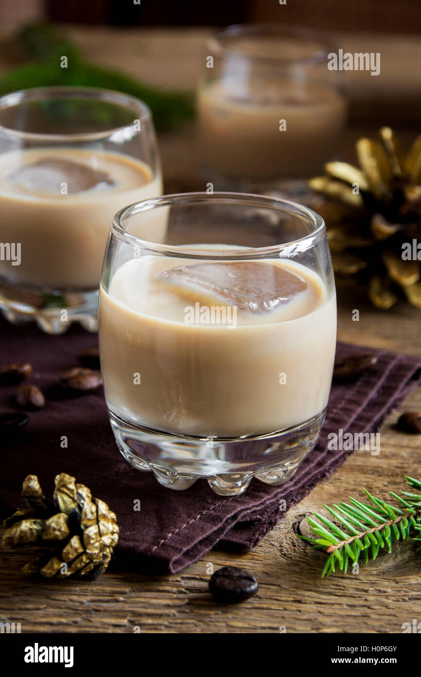 Irish cream coffee liqueur with ice, Christmas decoration and ornaments over rustic wooden background - homemade festive drink Stock Photo