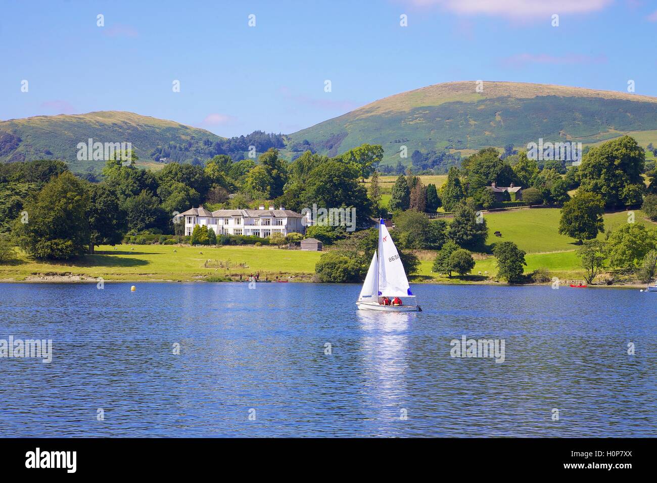 White sailed boat sailing past Rampsbeck Hotel. Ullswater, Penrith, The Lake District National Park, Cumbria, England, UK. Stock Photo