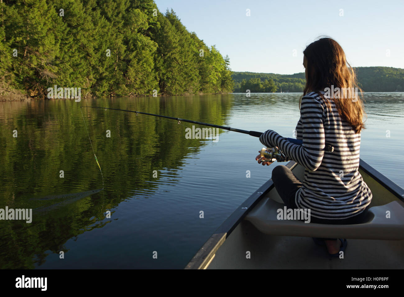 Girl with fishing rod in a canoe on a lake in Vermont as the sun rises Stock Photo
