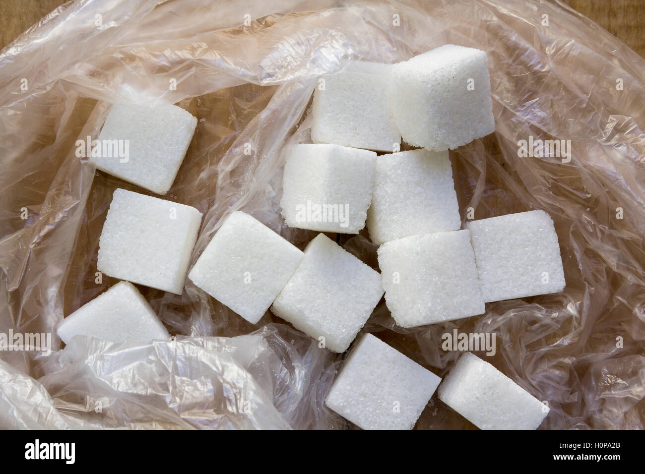 White sugar pieces in a plastic bag on a wooden background. Stock Photo