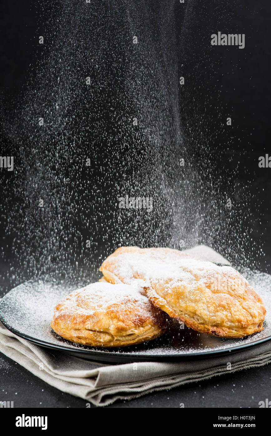 Sprinkling powdered sugar on cakes on a black background Stock Photo