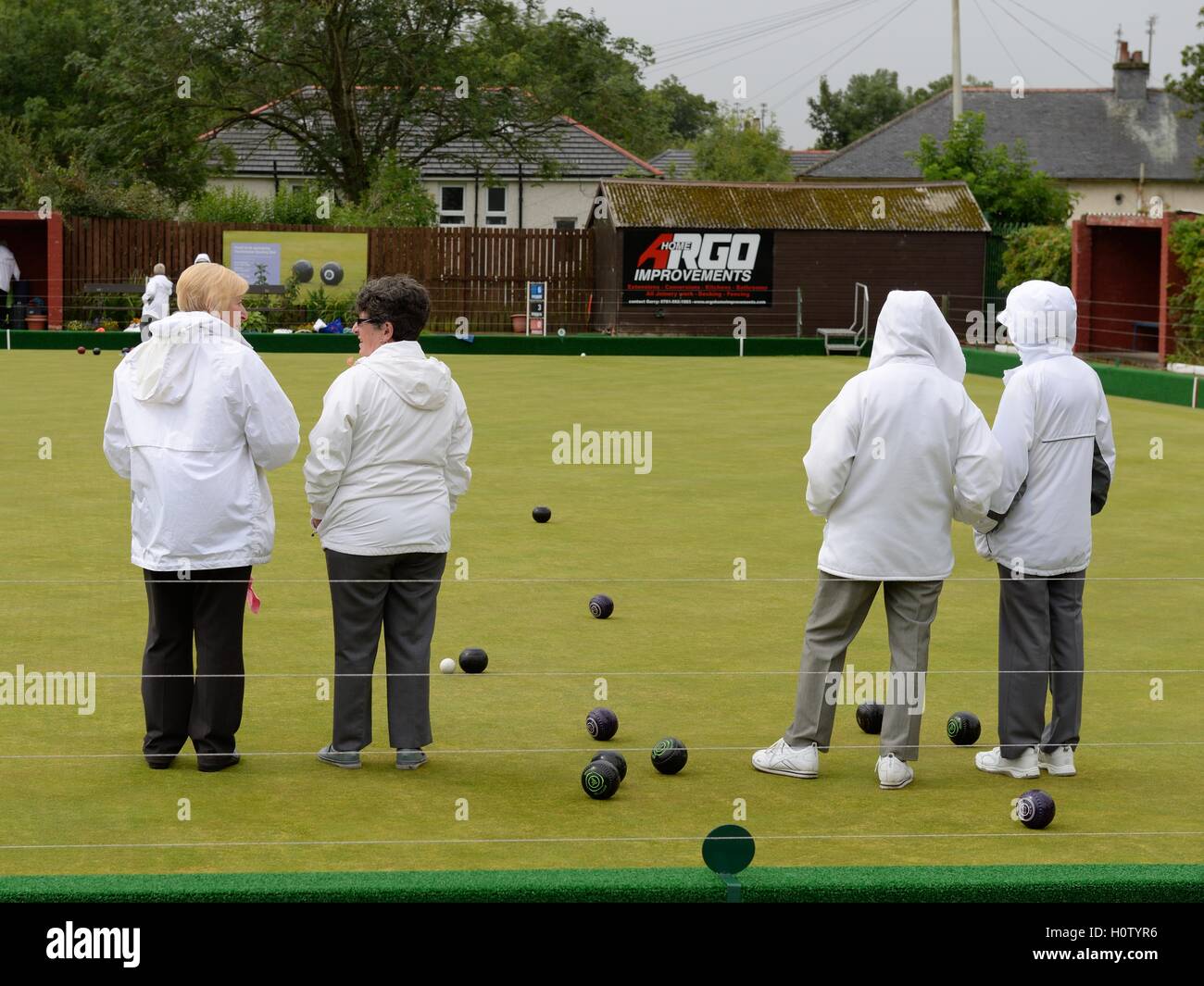 Women lawn bowlers wearing traditional white jackets in inclement weather. Stock Photo