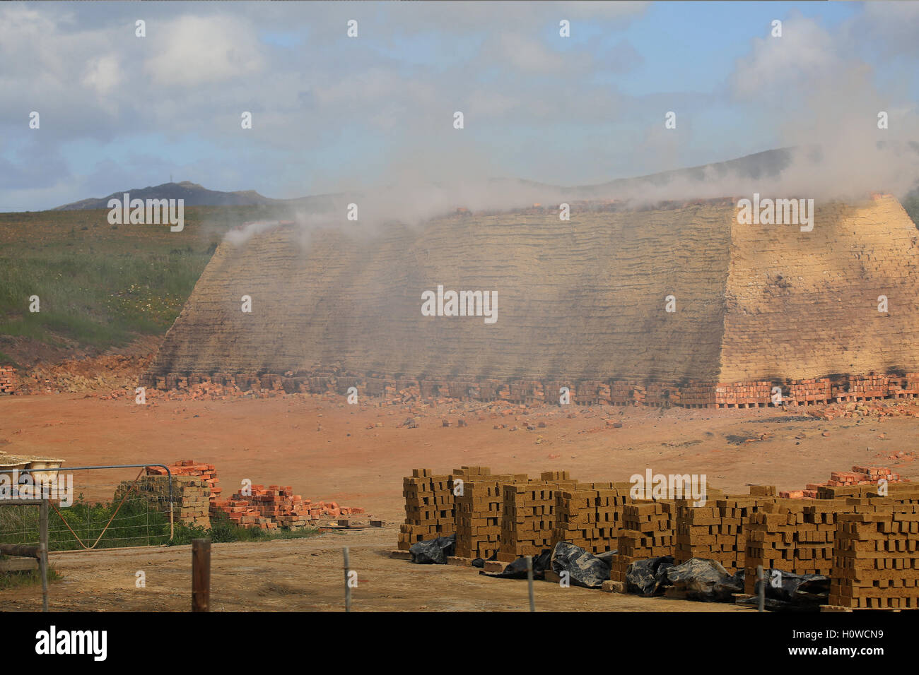 A smoking brickyard with a pyramid of baking bricks using the clamp