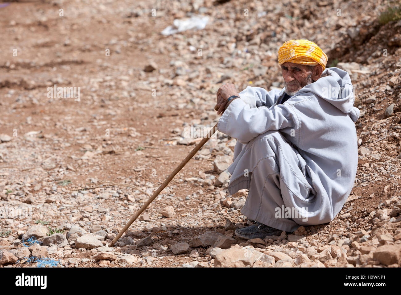 Atlas Mountains, Morocco.  Market Scene in Village near Dades Gorge.  Man Resting with his Walking Stick. Stock Photo
