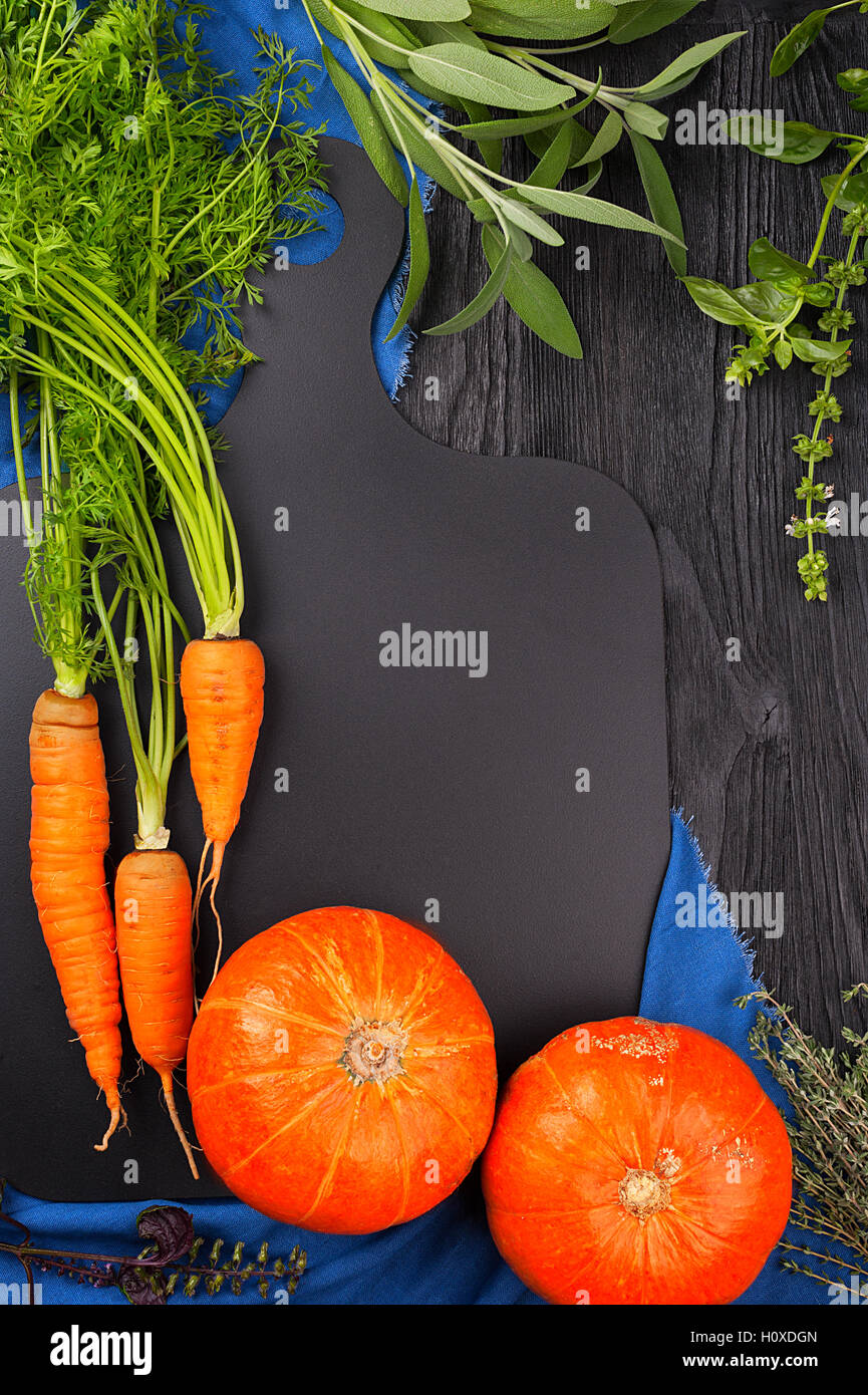 Carrots, pumpkin, sage, basil and thyme on a blackboard and a blue towel top view with copy space Stock Photo