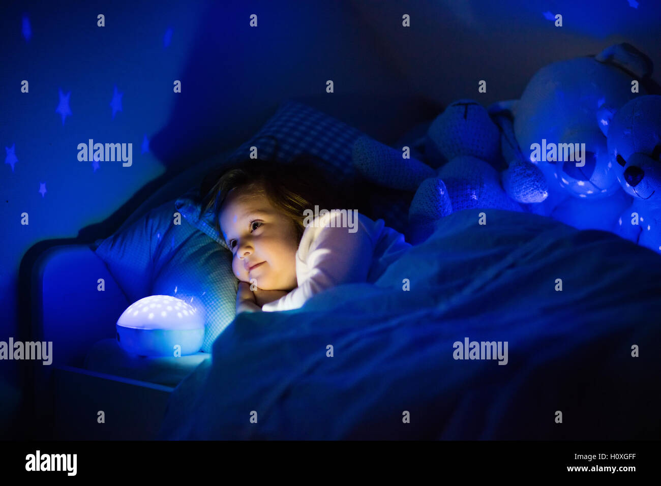 Little girl reading a book in bed. Dark bedroom with night light