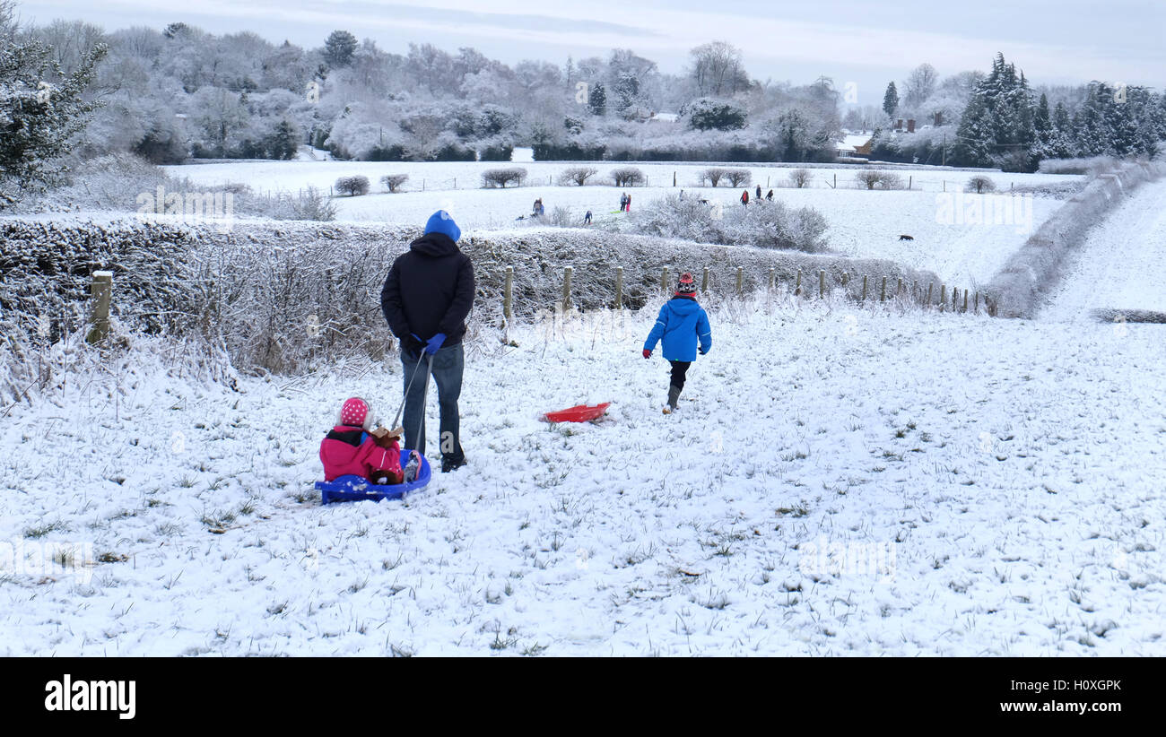 Snowy country scene - A father sets out across a snow covered field with two children and their sledges Stock Photo